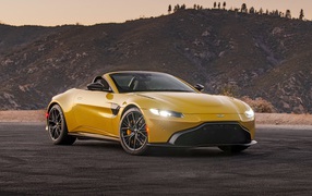 Желтый автомобиль  Aston Martin Vantage Roadster, 2021 года на фоне холмов