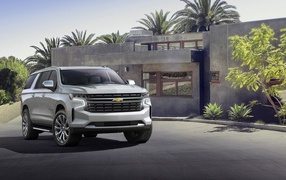 Серый внедорожник Chevrolet Suburban, 2021 года на фоне дома