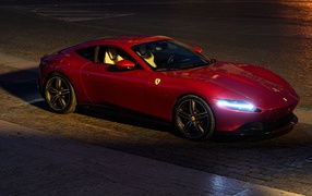 Красный автомобиль Ferrari Roma 2020 года с включенными фарами вечером