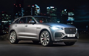 Серебристый Jaguar F-Pace R-Dynamic 2020 года на фоне ночного мегаполиса 