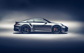 Серебристый автомобиль Porsche 911 Turbo S 2020 года вид сбоку на сером фоне
