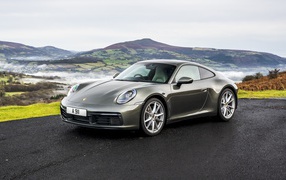 Серебристый автомобиль Porsche 911 Carrera на фоне холмов