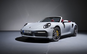 Белый кабриолет Porsche 911 Turbo S 2020 года на сером фоне