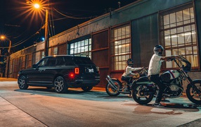 Черный автомобиль Rolls-Royce Cullinan, 2020 года у гаража с байкерами