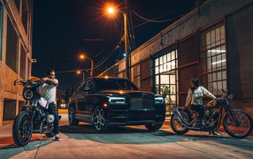 Черный стильный автомобиль Rolls-Royce Cullinan на улице города с байкерами