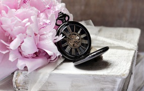 Черные карманные часы с книгой и цветами на столе 