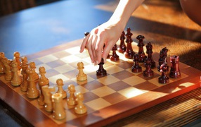 Женская рука переставляет шахматы на доске 