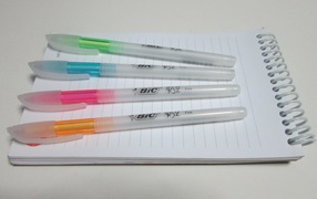 Разноцветные ручки лежат на блокноте на белом фоне 