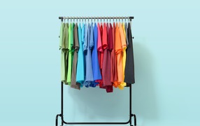 Разноцветные футболки на вешалке на голубом фоне