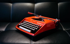 Старая красная печатная машинка на черном диване