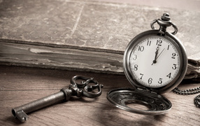 Карманные часы на столе с ключом и старой книгой 
