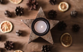 Свеча в форме звезды на столе с шишками и сушеным апельсином