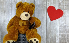 Плюшевый медведь с красным сердцем на деревянном фоне