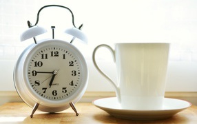 Белый будильник и чашка кофе на утреннем столе
