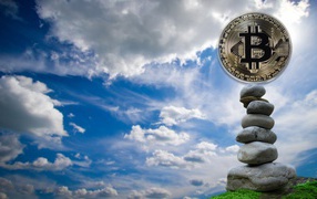 Bitcoin coin stands on stones against the background of the sky