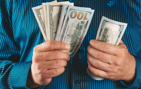 Мужчина считает сто долларовые купюры 