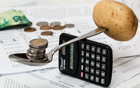 Весы из калькулятора и ложки с монетами и картофелем