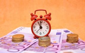 Маленький красный будильник с купюрами евро и монетами