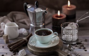 A cup of espresso on a table with cinnamon, marshmallows and candles
