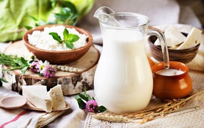 A jug of milk stands on a table with cheese and cottage cheese