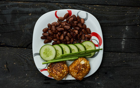 Фасоль на тарелке с оладьями и огурцами 