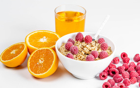 Bowl of muesli with raspberries and oranges on a table with juice