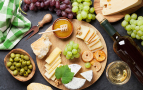 Cheese on a table with grapes, olives and white wine
