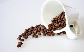 Кофейные зерна высыпают из белой чашки на стол 