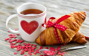 Croissant on a table with a cup of tea and hearts