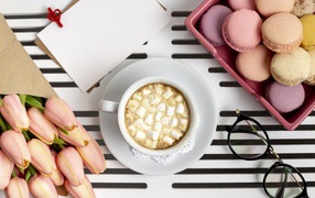 Чашка какао с маршмеллоу на столе с букетом тюльпанов, десертом макарун и очками