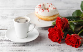 Чашка кофе, пончик и три красных розы на столе