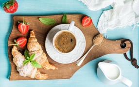 Cup of coffee on a board with strawberries and croissants