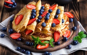 Delicious thin pancakes on a wooden board with blueberries and strawberries