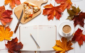 Diary on table with yellow leaves, coffee and pizza