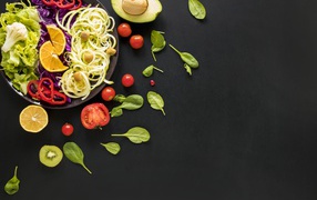 Салат из свежих овощей на черном столе с базиликом, помидорами и авокадо 