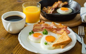 Fried eggs with bacon and toast on a table with juice and coffee