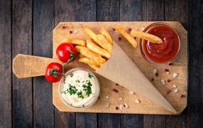 Ketchup, sauce and french fries on a board with tomatoes