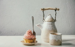 Kettle with a cup on a table with a cupcake