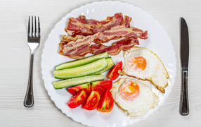 Large white plate with bacon, cucumbers, tomatoes and fried eggs