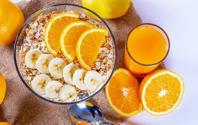 Овсяные хлопья в тарелке с кусочками банана и апельсина на столе с соком