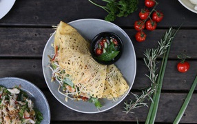 Блин с салатом на тарелке на столе с помидорами