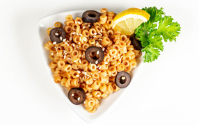 Макароны на тарелке с оливками и лимоном