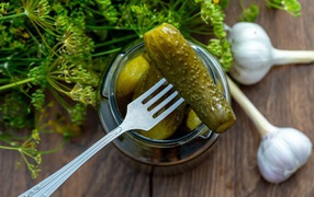 Маринованные огурцы в банке на столе с чесноком и укропом