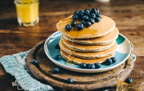 Ruddy pancakes on a plate with honey and blueberries