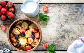 Маленькие оладьи в миске с клубникой и черникой на столе с молоком 