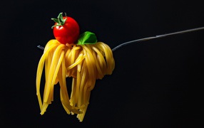 Spaghetti with tomato on a fork on a black background