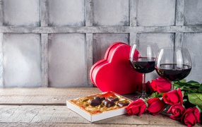 Два бокала вина, шоколадные конфеты и розы на столе для любимой 