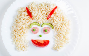 Лицо из вермишели с овощами и колбасой на белой тарелке 