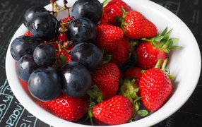 Синий виноград на тарелке с ягодами клубники 