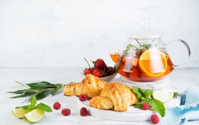Чайник с лимоном и клубникой на столе с круассанами 